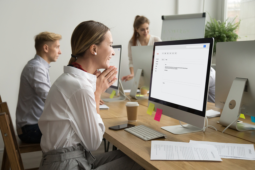 Woman sitting in front of a desktop computer smiling.